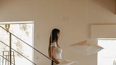 Photo of a hotel room. In the middle is a staircase down which a woman is walking.
