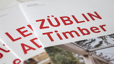 Foto von drei Coverseiten der Broschüren von ZÜBLIN Timber. Man sieht große, rote Aufschriften 