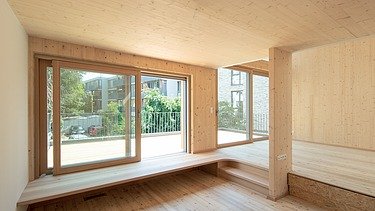 Foto eines Wohnhauses aus Holz. Unmöbliertes Wohnzimmer mit vielen Holzoberflächen.