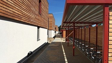 Foto des Studentenwohnheimes in Golm. Man sieht mehrere Holzgebäude und einen Fahrradüberstand.
