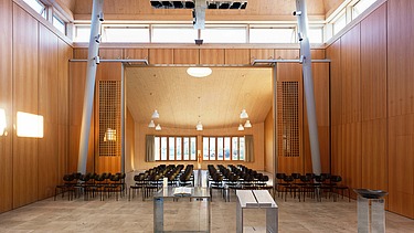  Foto der Kirche Burgweinting von innen. Zu sehen ist ein bestuhlter Innenraum und viele Holzoberflächen.