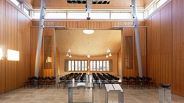  Foto der Kirche Burgweinting von innen. Zu sehen ist ein bestuhlter Innenraum und viele Holzoberflächen.