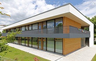 Außenaufnahme der Kita in Frankfurt. Man sieht ein Gebäude aus Holz mit Flachdach.