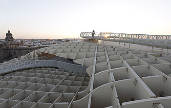 Photo of a skywalk of the Metropol Parasol in Seville Spain. You can see a person standing on the skywalk at dusk.