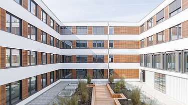 Foto des Bürogebäudes Flexim Berlin von außen. Zu sehen ist ein großes U-förmiges Gebäude aus Holz mit Holz-Putzfassade und Flachdach.