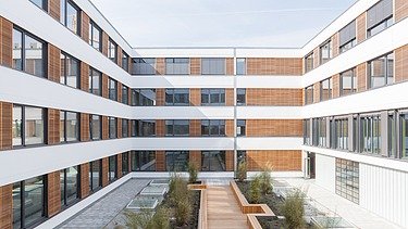 Photo of the Flexim Berlin office building from the outside. You can see a large U-shaped building made of wood with a wooden plaster façade and flat roof.