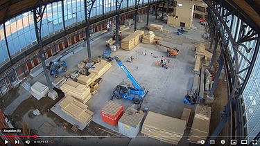 Photo of a hall in the Gare Maritime in Brussels. You can see many stacks of wood and vehicles.