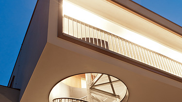 Night shot of a section of a building with external spiral staircase. Wooden extension.