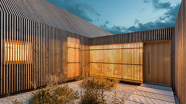 Foto eines modernen Holzhauses in U-Form mit Holzfassade. LENO-BSP.
