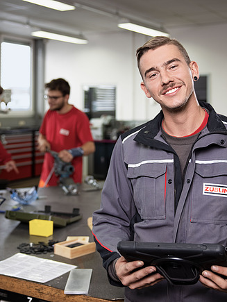 Bild eines jungen Mannes in Arbeitskleidung, der ein Tablet in der Hand hält und lächelt