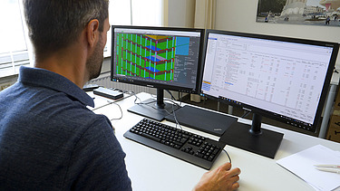 Photo of a colleague from ZÜBLIN Timber sitting at a computer workstation. 
