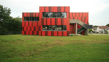 Foto einer Außenansicht der Einhardschule in Seligenstadt. Man sieht eine rote Fassade.