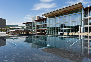 Foto des Hotels Aqualux ini Bardolino. Zu sehen ist ein großes Gebäude mit Glasfassade und Flachdach, zudem ein Pool.