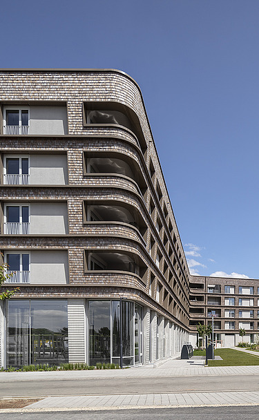 BUGA-Areal Spinelli, Mannheim. Zu sehen ist hier der Holz-Hybrid-Bau B9.1 Foto eines großen mehrgeschossigen Gebäudes mit Holzfassade. BUGA-Areal Mannheim.
