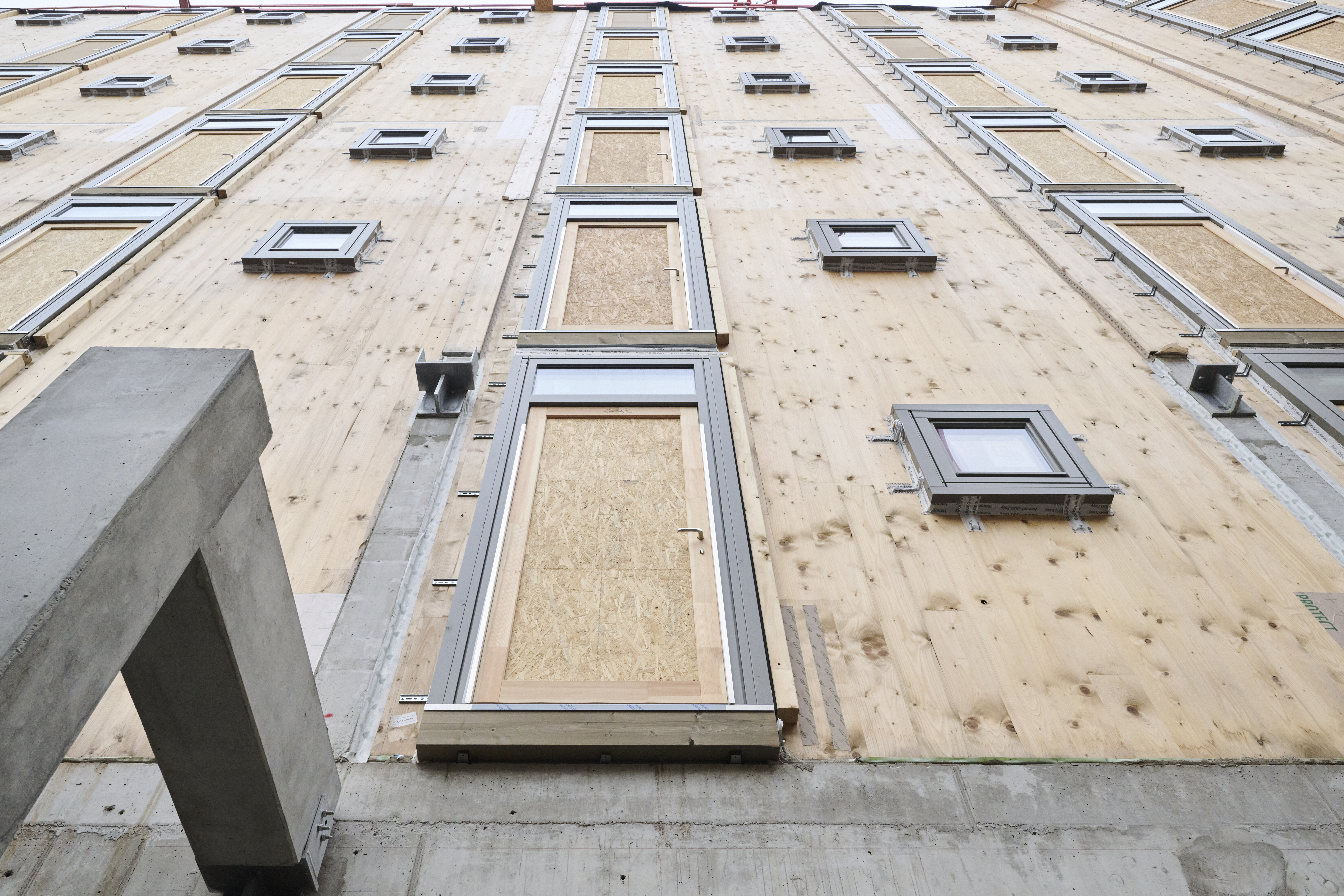 Foto eines mehrgeschossigen, hohen Holzgebäude, mit Blick an der Holzfassade nach oben.