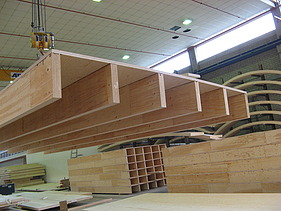 Photo of a rib element on the crane in the ZÜBLIN Timber production hall. Box elements can also be seen in the background.