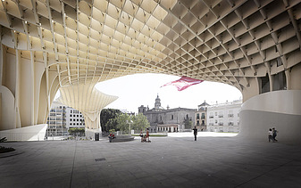 Photo of the marketplace canopy of the Metropol Parasol Sevilla. People are standing under a mushroom-like wooden construction.