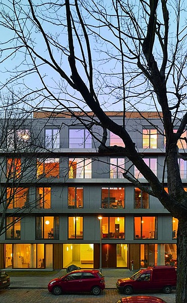 3xGRÜN, Berlin Photo of a multi-storey building in dim light. Leafless trees stand in front of it.