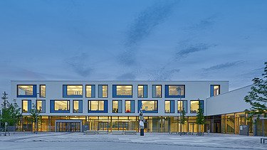 Exterior shot of the Munich North Grammar School. You can see a large, white building with a flat roof in a dusky evening atmosphere.