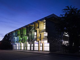 Night shot of a school building with colorful façade elements made of laminated veneer lumber.