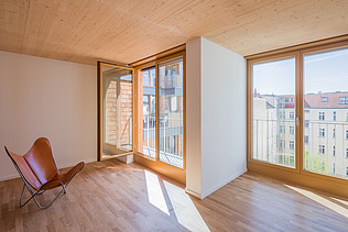Photo of an interior with a wooden ceiling and large windows and a red chair inside.
