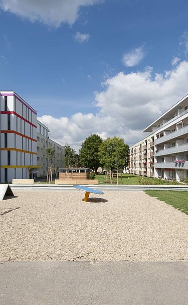 Aufstockung Konradsiedlung, Regensburg Foto zweier mehrgeschossigen Gebäude mit Garten davor. Aufstockungen aus Holz.