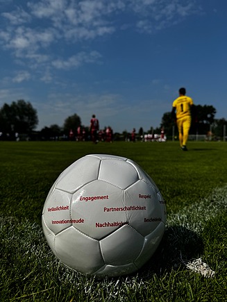 Foto mit einem weißen Fußball auf dem Rasen. Auf dem Fußball stehen in roter Schrift die ZÜBLIN-Werte.