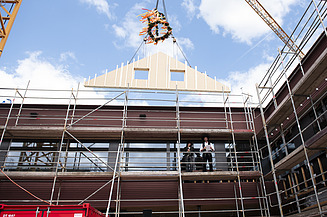 News ZÜBLIN Timber Photo of a wooden gable wall element suspended from a crane above the Schule am Hangs in Frankfurt.