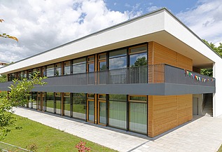 Außenaufnahme der Kita in Frankfurt. Man sieht ein Gebäude aus Holz mit Flachdach.