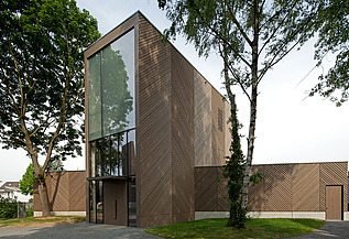 Foto einer Außenaufnahme der Immanuelkirche in Köln. Diese hat eine Holzfassade und ein Flachdach und einen je seitlichen Anbau aus Holz.