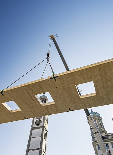 Photo of a floating LENO cross-laminated timber element on the crane. Blue sky. 