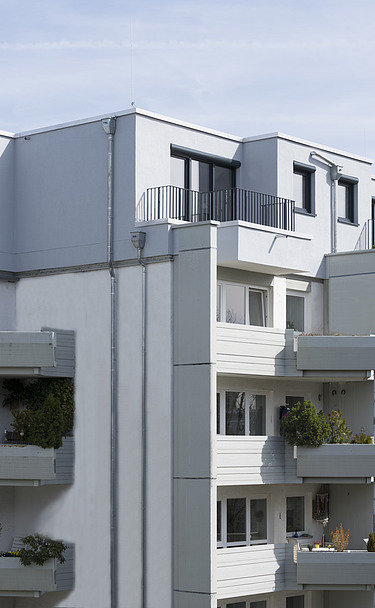 Foto eines mehrgeschossigen Gebäudes mit weißer Fassade. Aufstockung aus Holz.