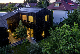 Foto eines Wohnhauses aus Holz und mit dunkler Holzfassade. Abendstimmung.