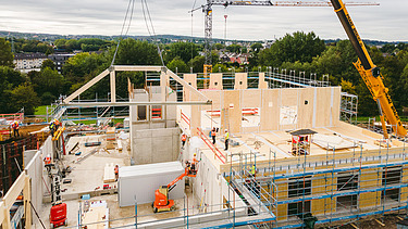 Foto der Uni Witten von außen. Man sieht die Montage großer Holzelemente.