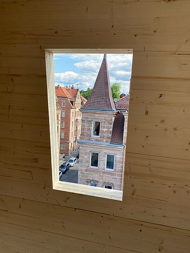 Foto einer LENO-Brettsperrholz-Wand mit einem Fenster. Darin ist ein Kirchenspitz zu erkennen.