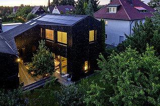 Foto eines Wohnhauses aus Holz und mit dunkler Holzfassade. Abendstimmung.