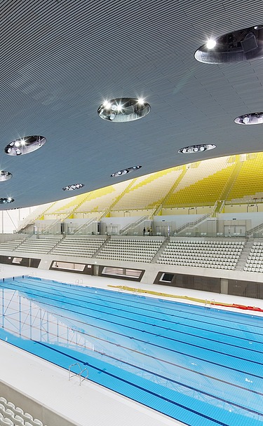 Aquatics Centre London Foto des Aquatics Centres in London von innen. Zu sehen ist die Holzdachkonstruktion und ein großes Schwimmbecken.