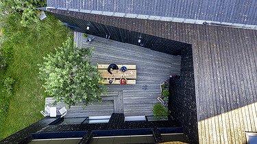 Foto eines Wohnhauses aus Holz und mit dunkler Holzfassade. Blick von oben auf die Terrasse.