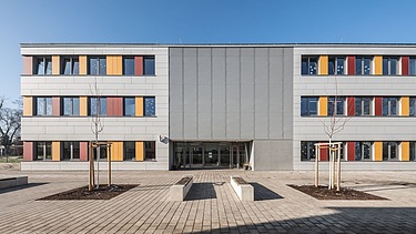 Außenaufnahme der Schule in Erfurt. Man sieht ein großes, weißes Gebäude mit bunten Farbelementen bei den Fenstern.