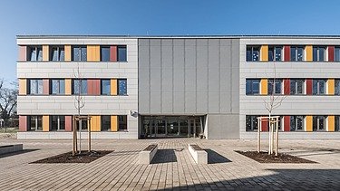 Außenaufnahme der Schule in Erfurt. Man sieht ein großes, weißes Gebäude mit bunten Farbelementen bei den Fenstern.