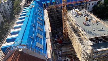Foto des Rohbaus VINZENT in München. Zu sehen ist ein eingerüstetes, mehrgeschossiges Gebäude von oben.