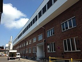 Photo of a multi-storey building. Wooden extension with white façade and flat roof.