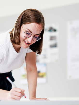 Photo of a draughtswoman trying to write on a plan.