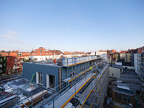 Foto des Rohbaus VINZENT in München. Zu sehen ist ein eingerüstetes, mehrgeschossiges Gebäude.