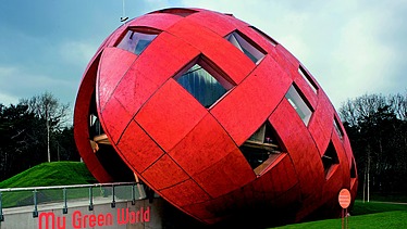 Foto eines rießigen, schrägliegenden Holzeis mit orangefarbiger Holzfassade und Fenstern.