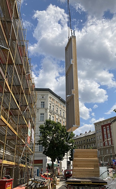 Foto der Holzbaumontage in der Stendaler Straße in Berlin. Man sieht ein großes LENO-ADD-Holzelement am Kran.