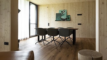 Foto eines Wohnraumes mit viel Holzoberflächen. Tisch, Stühle und Hocker.