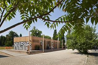 Foto eines Holzgebäudes mit Flachdach. Zu sehen ist auch ein Graffiti auf der Holzfassade.