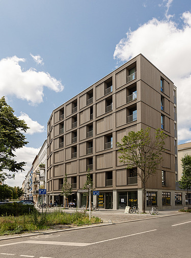 Foto der mehrgeschossigen Wohnanlage in der Stendaler Straße Berlin. Man sieht ein hohes Gebäude mit Holzfassade.