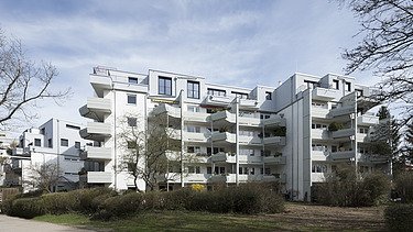 Foto eines mehrgeschossigen Gebäudes mit weißer Fassade. Aufstockung aus Holz.